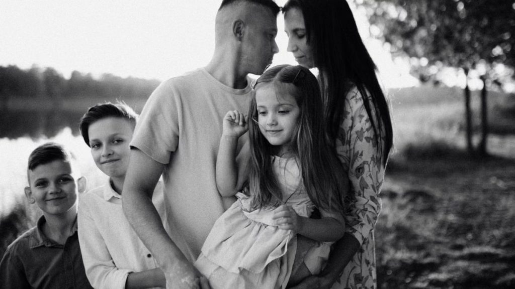 A serene black and white portrait of a family standing by a lake.