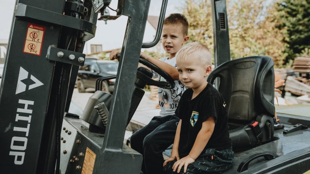 Two young boys explore a stationary vehicle outdoors, embodying play and curiosity.